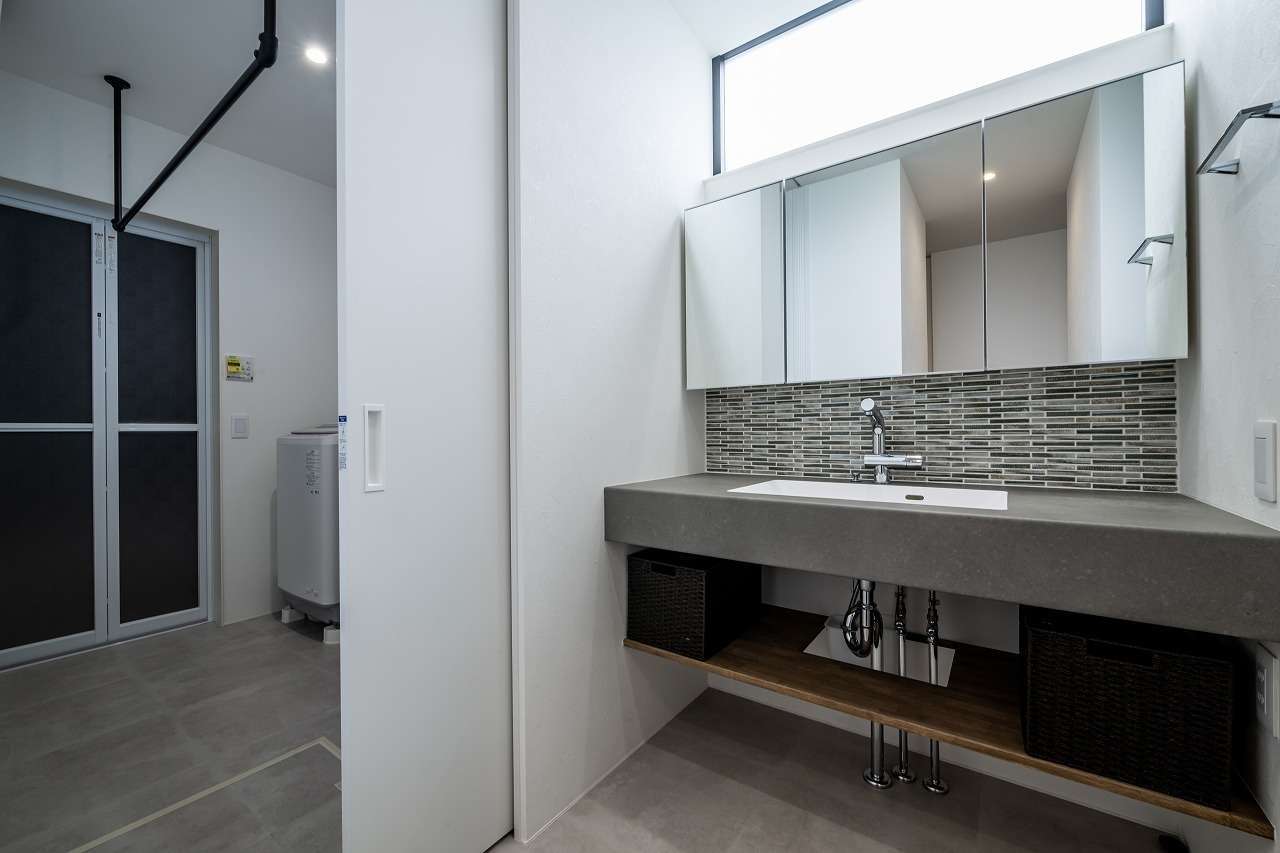 アーキテックス【デザイン住宅、省エネ、平屋】ランドリールームとファミリークローゼットの中間に設置した洗面台。無機質なモールテックスの質感にワイドな鏡とタイルがベストマッチ