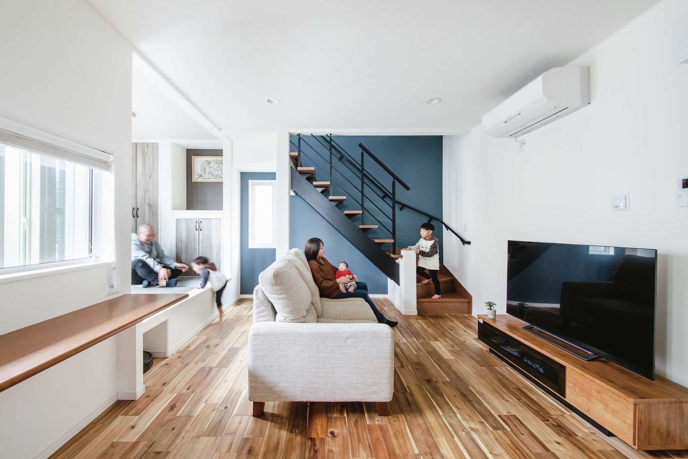 子育て安心住宅 Design Craft Office【デザイン住宅、子育て、狭小住宅】アイアンのオープン階段とブルーグレーのアクセントクロスがマッチしたLDK。ご主人の要望で、床には無垢材を使用。スタディカウンターの外側には中庭デッキがある。浴室を2階に配置してLDKの広さに余裕を持たせたことで、小上がりの畳コーナーを設けることもできた
