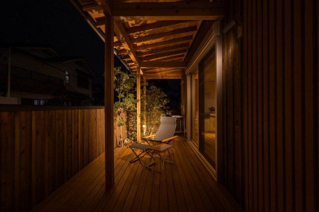 KEN建築工房｜夜のウッドデッキ。暖かな照明の下、リラックスできるアウトドア用の椅子が配置され、木の温もりが漂う。静かな夜のひとときを楽しむのに最適な空間です。