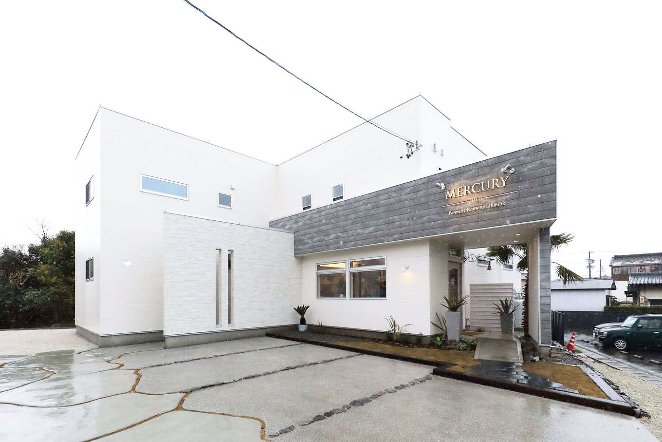 トーリンホーム【デザイン住宅、高級住宅、インテリア】グレーの外壁部分に店舗名が記され、その下が美容サロンへのアプローチとなっている。一方、住居の玄関アプローチは来客や周囲の視線に配慮して白い壁で隠し、プライバシーを確保した