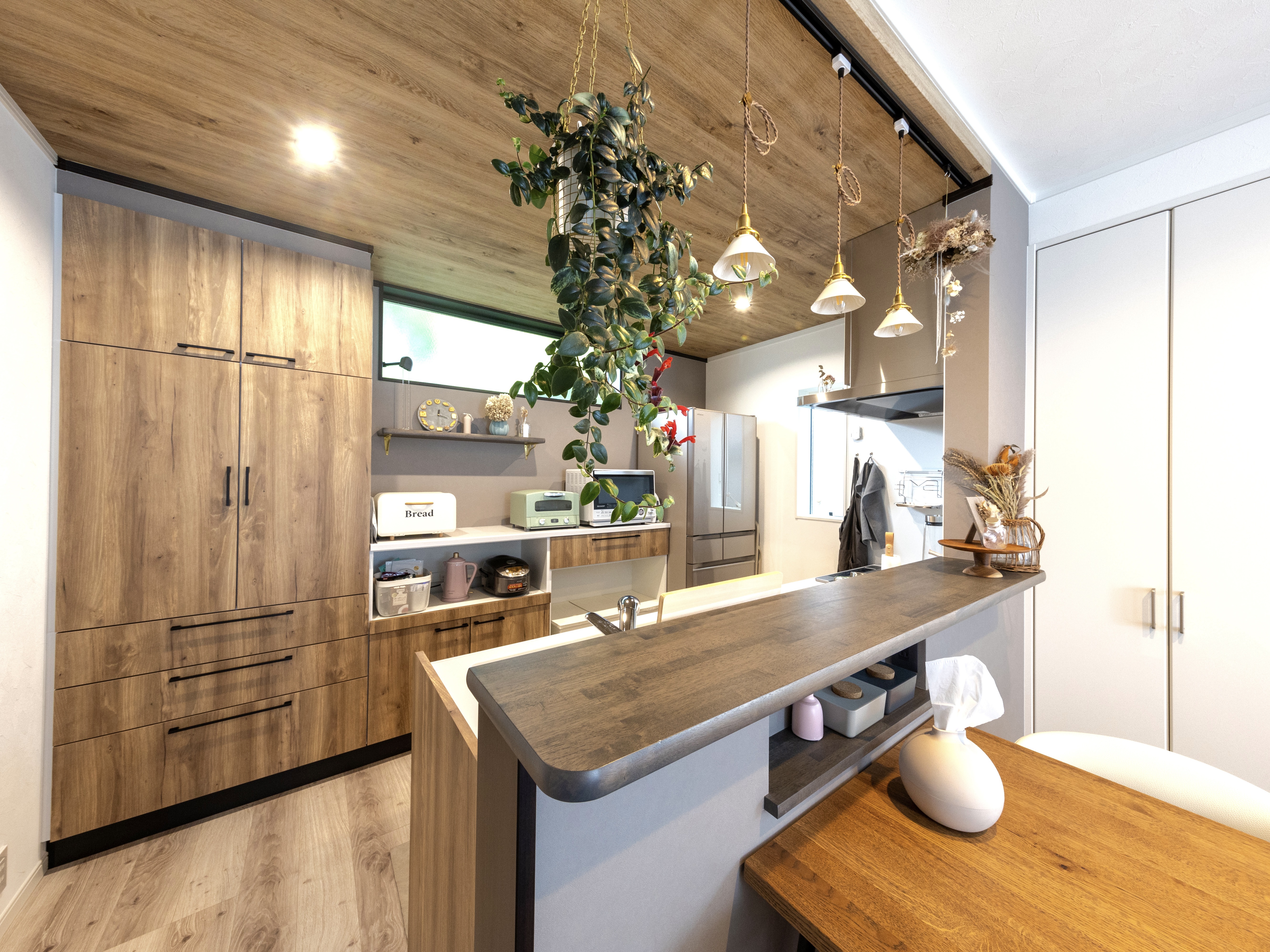 エスホーム｜木目調のインテリアが温かみを演出するキッチン。吊り下げられた照明が洗練された雰囲気を加え、収納が充実しているため機能的。