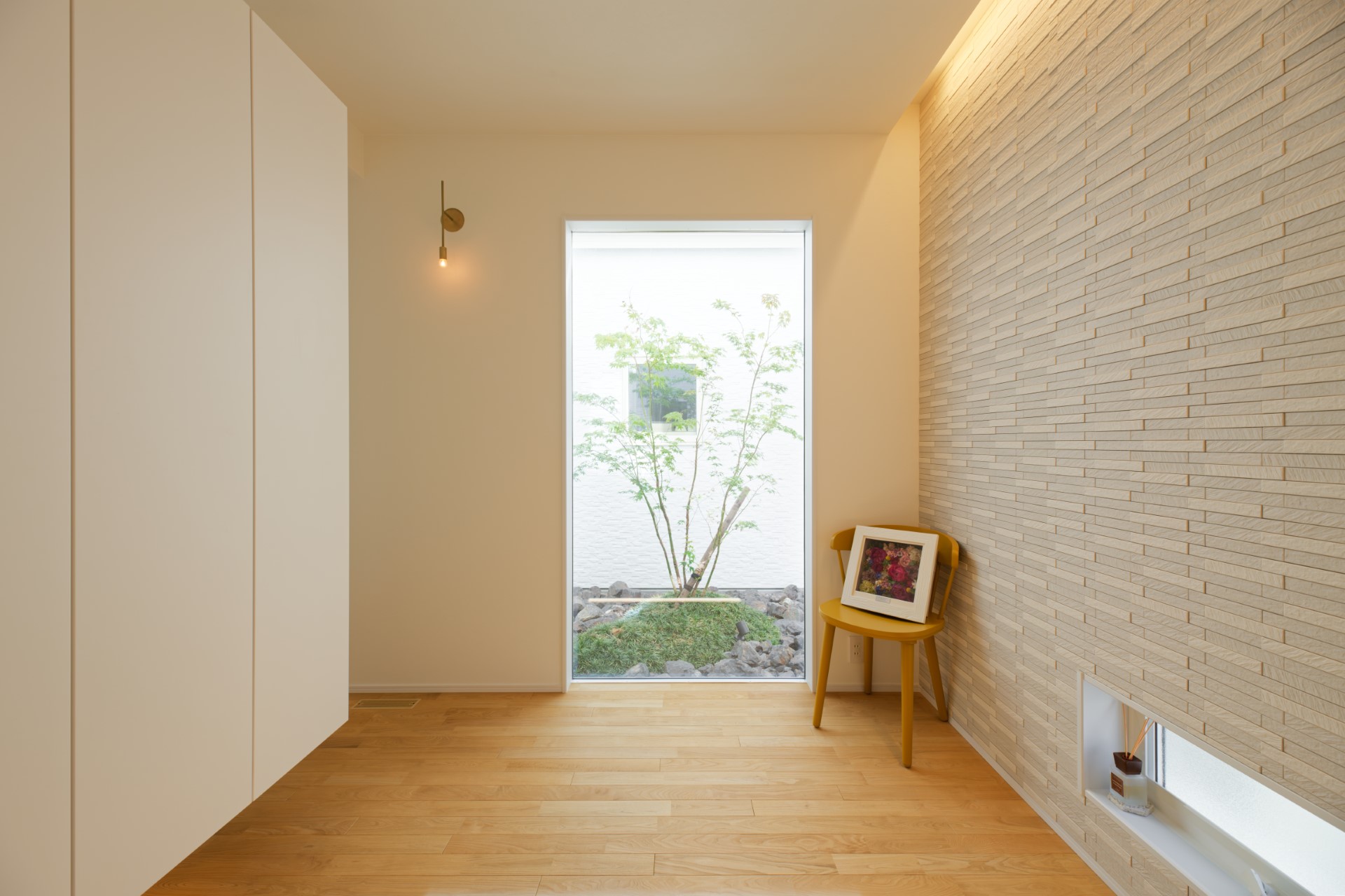 アサヒグローバルホーム｜その夢を形にするため、玄関正面に坪庭を設け、景色を印象的に切り取る大きなガラス窓をはめ込んだ。壁には陰影が美しく出るエコカラットをあしらっている