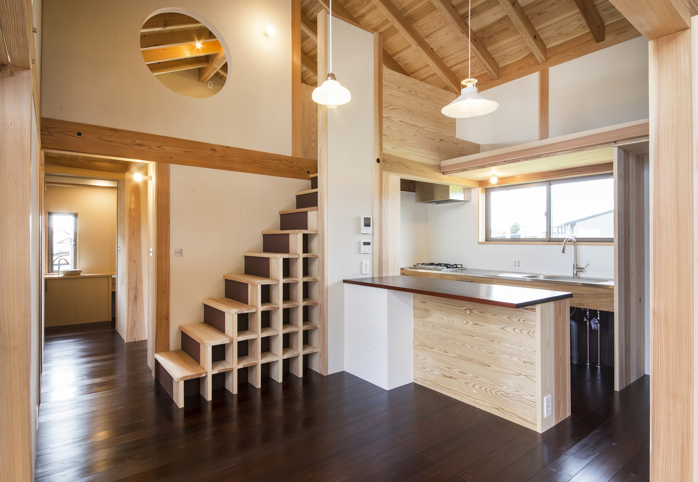 石牧建築【収納力、自然素材、建築家】カウンターキッチンは『石牧建築』のオリジナル造作。北面の景色を見ながら料理できるよう、I型キッチンと作業台を別々に。ここからパントリー、洗面脱衣所、トイレ、浴室、寝室へと回遊できる間取りになっている。箱収納付きの階段が空間のアクセントに