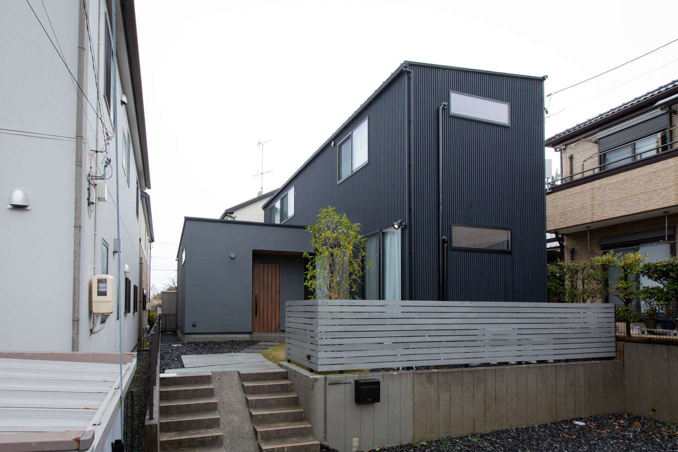 ハウスコネクト【デザイン住宅、間取り、建築家】高低差を利用して建てたI邸。駐車場と階段は建築前のまま。両隣の建物が近いため、視線が合わないよう窓の大きさと位置に配慮した。屋根にソーラーパネルを搭載し、光熱費を抑えた低燃費な暮らしを実現