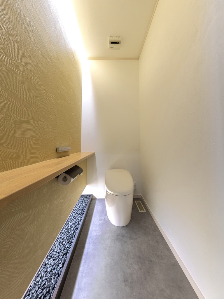 エスホーム｜高級飲食店風のトイレ。天井からの光が明るく柔らかい印象を与え、玉砂利を敷き、波のような模様の印象的なクロスにした。