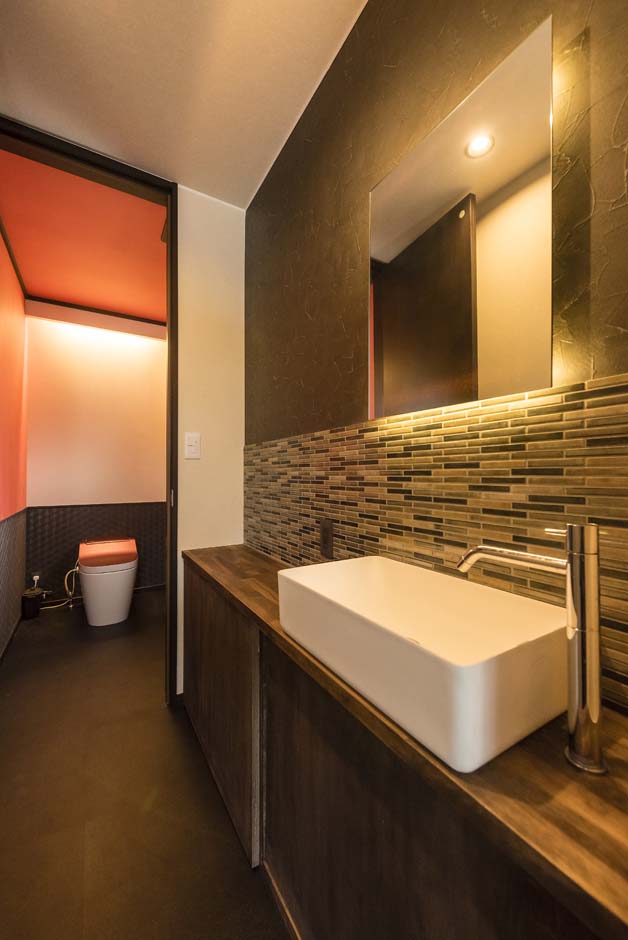 アトリエサクラ【デザイン住宅、間取り、ガレージ】モダンなタイル使いとの洗面台。トイレの天井にはアクセントカラーのオレンジのクロスを用いた