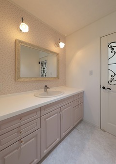 ライトピンクのキャビネットが可愛らしい洗面スペース。大きな鏡と明るい照明で、使い勝手の良いデザイン。