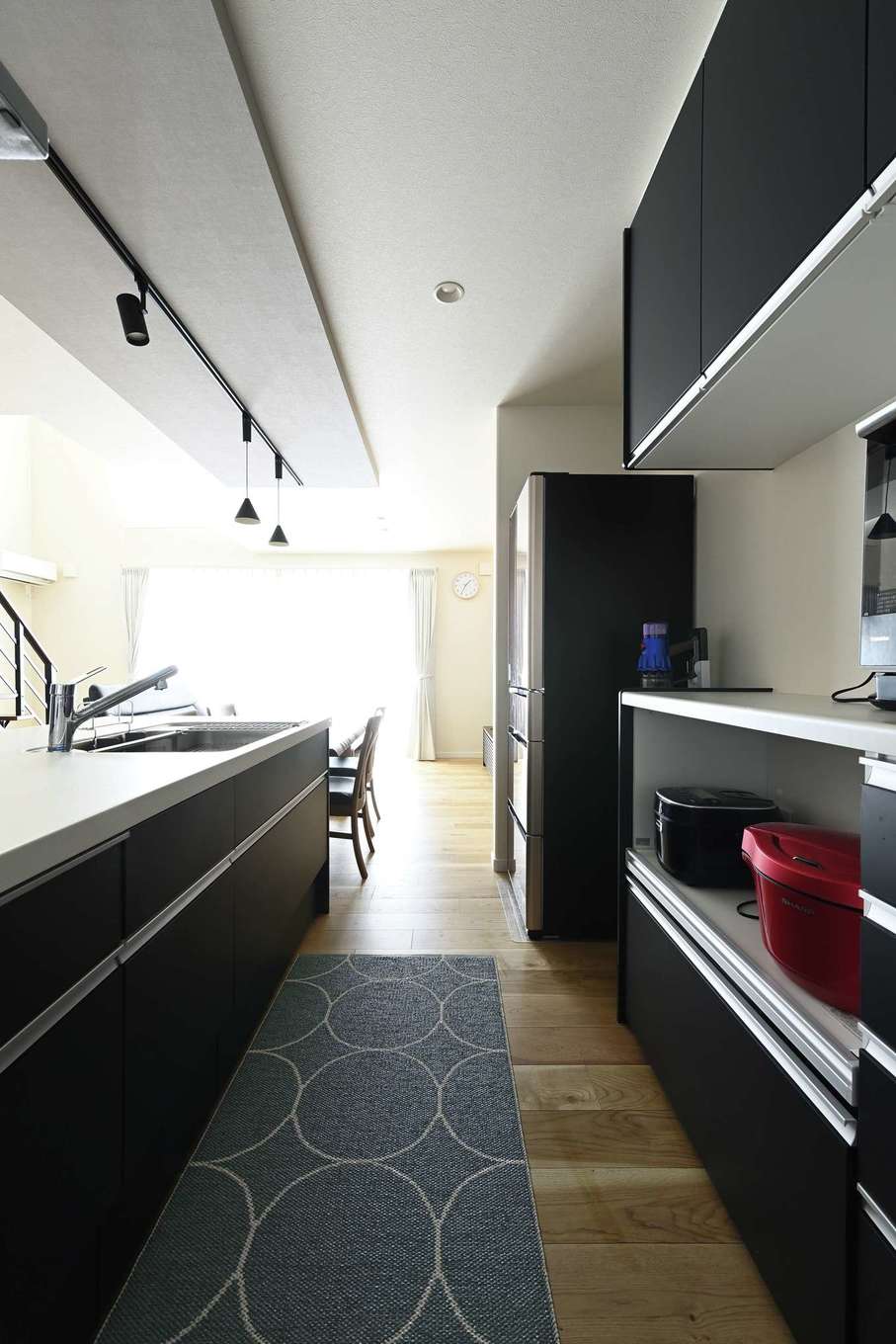 Yamaguchi Design 掛川店（アイフルホーム 掛川店）【デザイン住宅、子育て、間取り】下がり天井でアクセントを付けたキッチンスペース。対面キッチンとダイニングテーブルを並べて一直線に配置し、配膳や片付けの動線を短縮。キッチンの奥にはパントリーも設けている