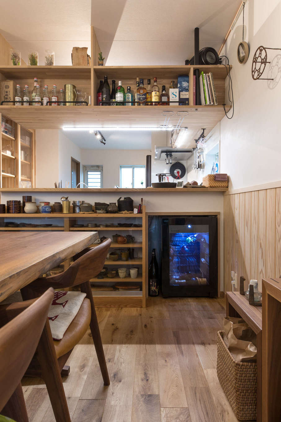 建築システム（狭小住宅専門店）【収納力、狭小住宅、鉄骨鉄筋コンクリート構造】キッチンの壁面を利用してダイニング側には豊富な茶器を収納するカップボードを造作。隣にはワインセラーを設けた。吊り収納はインテリア性も高いお酒のボトルをディスプレイ