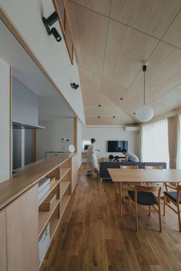 方形（ほうぎょう）の屋根の形を活かしたシナ合板張りの勾配天井が、縦の広がりを感じさせるLDK。ダイニングの造作棚にもシナ合板を採用。オークの無垢床とも調和して、シンプルで温かみのある空間が実現した