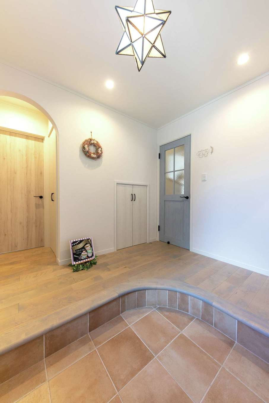 ハートホーム【デザイン住宅、自然素材、間取り】丸くカーブした玄関ホールの床。ホールを広く使えて、リビングドアが開けやすくなるメリットも。アールの下がり壁の内側にはコートをかける収納も。奥の扉から洗面室に行ける