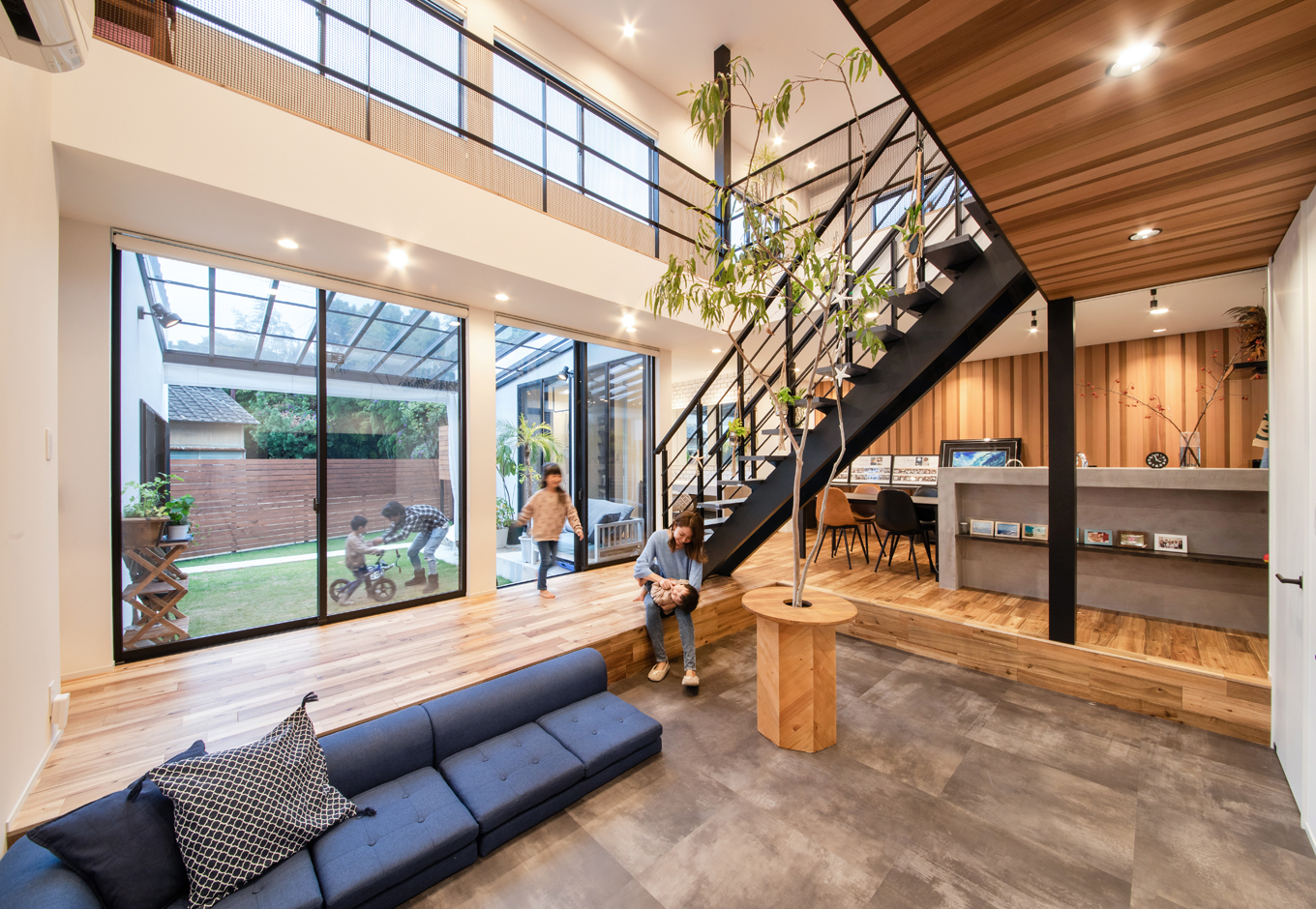 ハウスコネクト【デザイン住宅、収納力、建築家】大きな窓と吹き抜けが開放的なLDKは、ベンチがわりに座れる段差付きリビング、無垢アカシアの床、アイアンの階段がメリハリを生んでいる。「カーテンを使わない暮らしがしたい」と願う夫婦のため、西陽を遮るロールカーテンだけを取り付けている