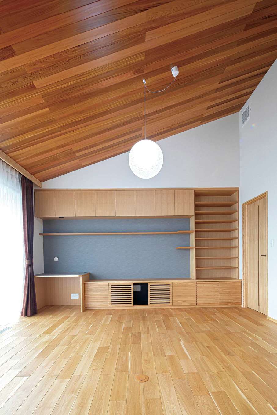 近藤建設工業【デザイン住宅、二世帯住宅、省エネ】勾配天井で縦空間の広がりを強調した子世帯のリビング。壁の一面は、スピーカーやAV機器を隠しながら設置できるテレビボードを兼ねたリビング収納を造作。空間が美しく整う