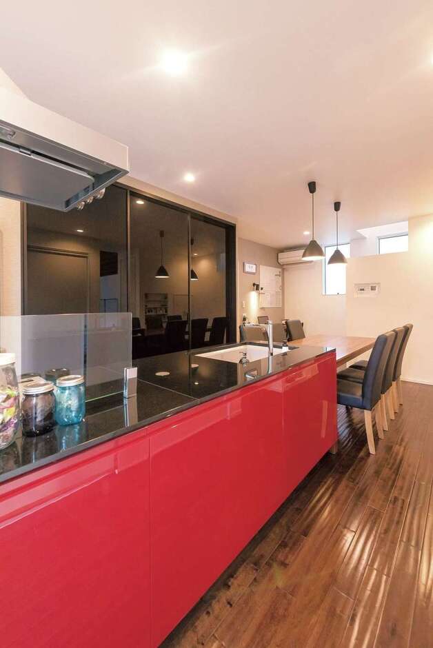 モノトーンの空間にイタリアンロッソ（赤）が映える『納得』オリジナルのキッチン。調理した料理をスムーズにコートテラスへ運べるので、BBQの準備、後片付けもラクラク。バックヤードの食器棚は引き戸でサッと隠せるので、不意の来客があっても安心