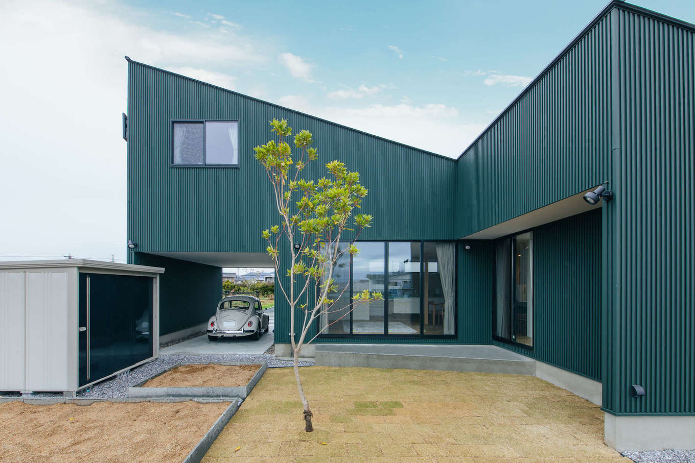 ハウスコネクト【デザイン住宅、建築家、ガレージ】南側から見た外観。広い庭をL字型に囲むように設計され、プライバシーを確保、ご主人が家庭菜園を楽しむための畑を2か所に設けた。タイルデッキでは、外からの視線を遮りながらBBQやプール遊びを楽しむことができる
