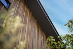 自然素材を活かした木目調の外壁が特徴の住宅の外観。爽やかな青空と緑の植物が調和し、温かみと落ち着きを感じさせる印象的なデザイン。