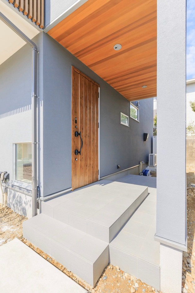 レッドシダー張りの天井と木扉がグレーの塗り壁に映える玄関アプローチ