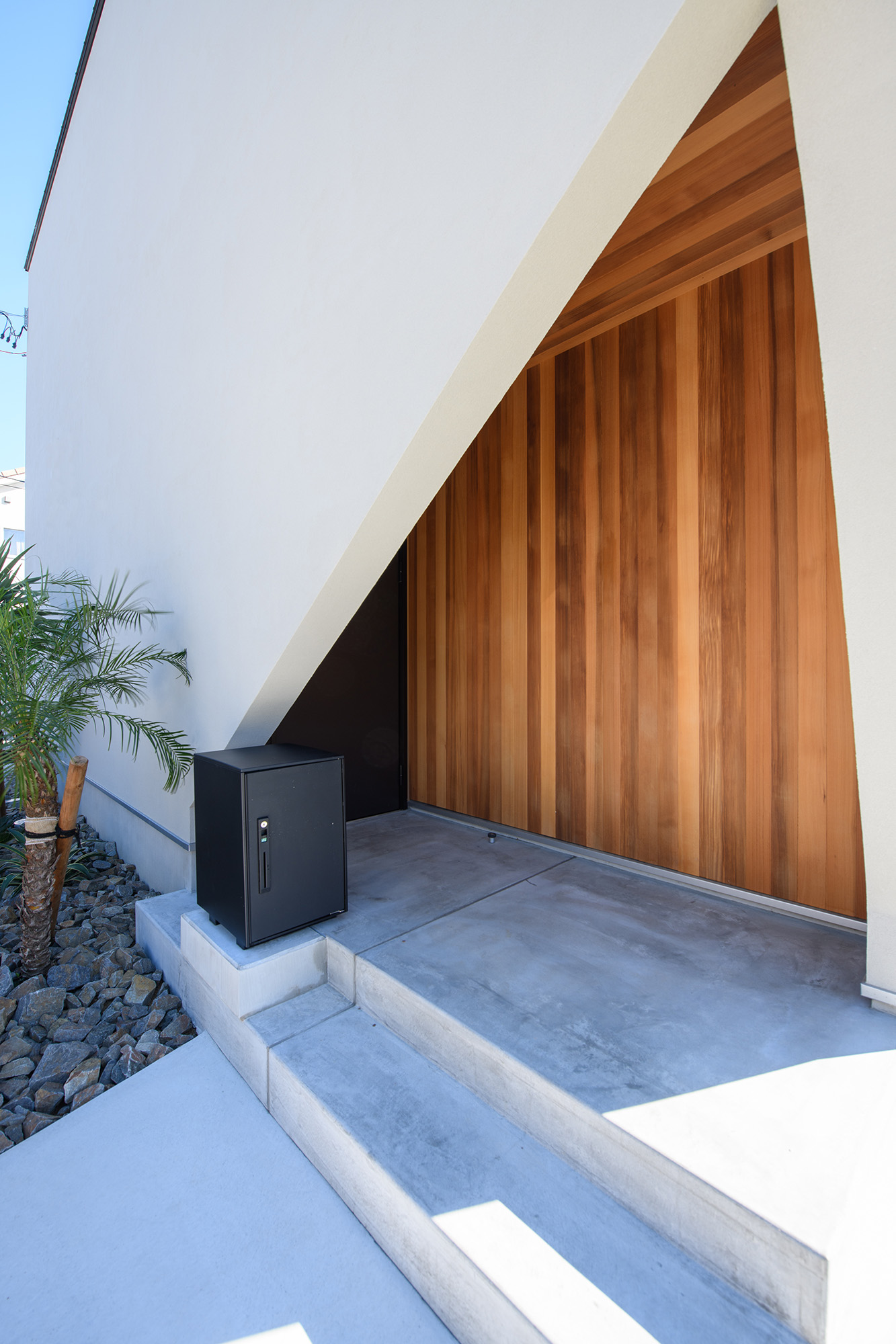 平屋建築ブルーハウス【デザイン住宅、間取り、建築家】玄関ポーチは内部の板張りの壁がアクセントとなり、白い箱型の外観を引き立てている。玄関ドアは正面からは見えないつくりで、プライバシーもしっかり保護できる