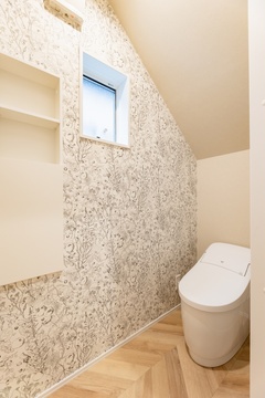 柄のある壁紙で個性的に仕上げられたトイレ空間。コンパクトながらも自然光が差し込み、開放感のあるデザインとなっている。床のヘリンボーン模様がアクセント。