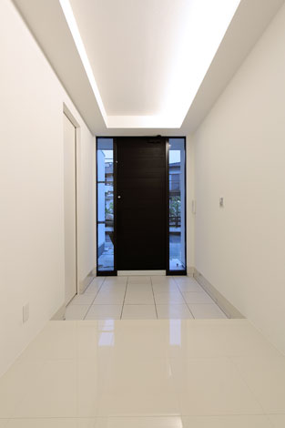 丸昇彦坂建設【デザイン住宅、間取り、ガレージ】天井の間接照明が優雅な雰囲気を演出する玄関。左側の扉の先は土間収納とガレージに通じている