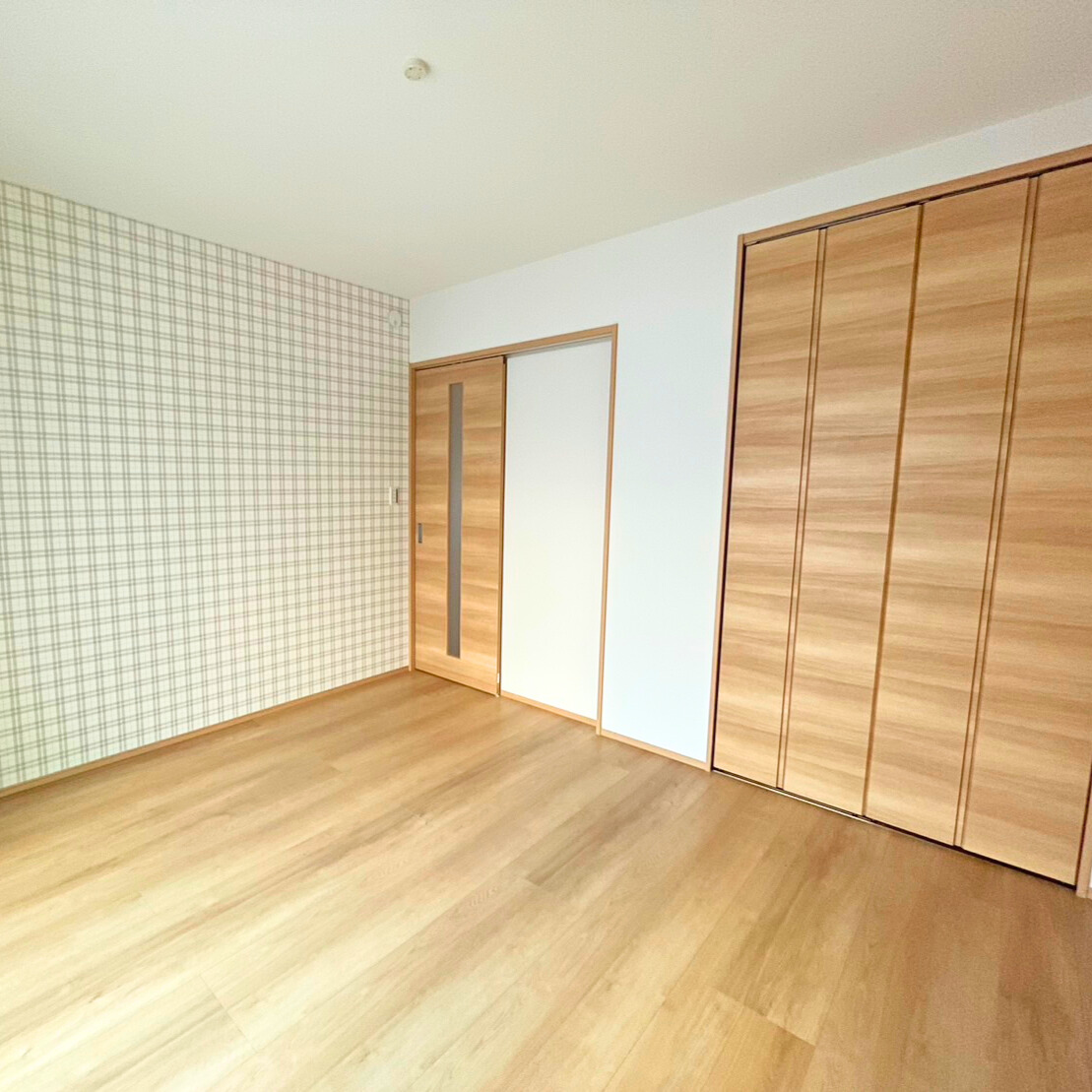 沢田建設｜明るいナチュラルカラーの床材を使用した居室。壁の一面にはアクセントとしてチェック柄のクロスが施され、洗練された雰囲気を演出している。広々としたクローゼットがあり、収納力も抜群である。