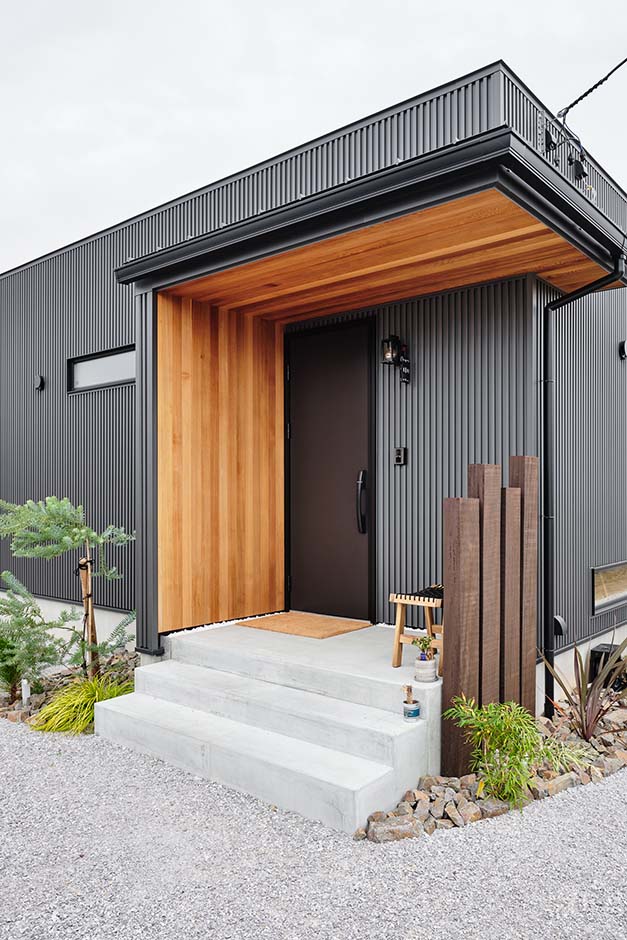 平屋建築ブルーハウス【ペット、建築家、平屋】無垢のレッドシダーと植栽が、あたたかみを醸す玄関。視線をさりげなくカットする枕木フェンスにもセンスが光る