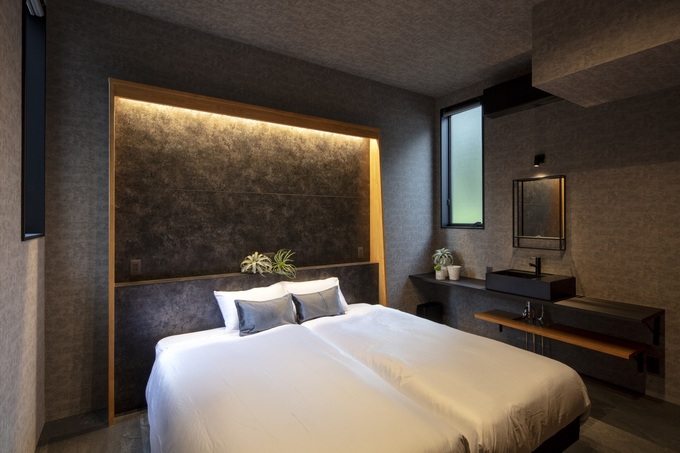 シックなデザインでまとめた寝室。落ち着いた照明とシンプルなインテリアが安らぎを演出している。ベッド脇の洗面スペースも機能的。