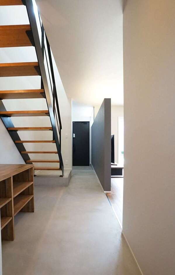 土間仕上げのスタイリッシュな玄関ホール。LDKとフラットにつなげたことで空間に一体感が生まれ、広く感じられる。さらに、階段をスケルトンにしたことによって視線が抜け、より開放的な雰囲気に。完全に間仕切りしていないので、リビングからの光が届いて明るさも確保