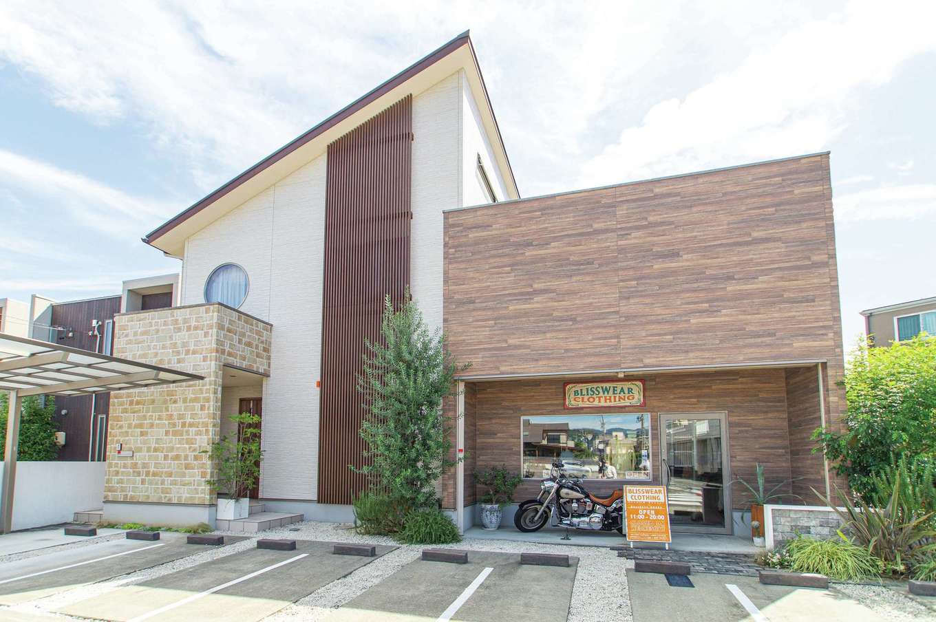 さくらホーム【デザイン住宅、収納力、間取り】店舗前のハーレーがご主人の営む「BLISSWEAR CLOTHING」の目印。住居部分は片流れのシャープなフォルムに、目隠しとしても機能する格子の縦ラインと丸い窓がアクセント。建物にあわせて依頼した外構もマッチ