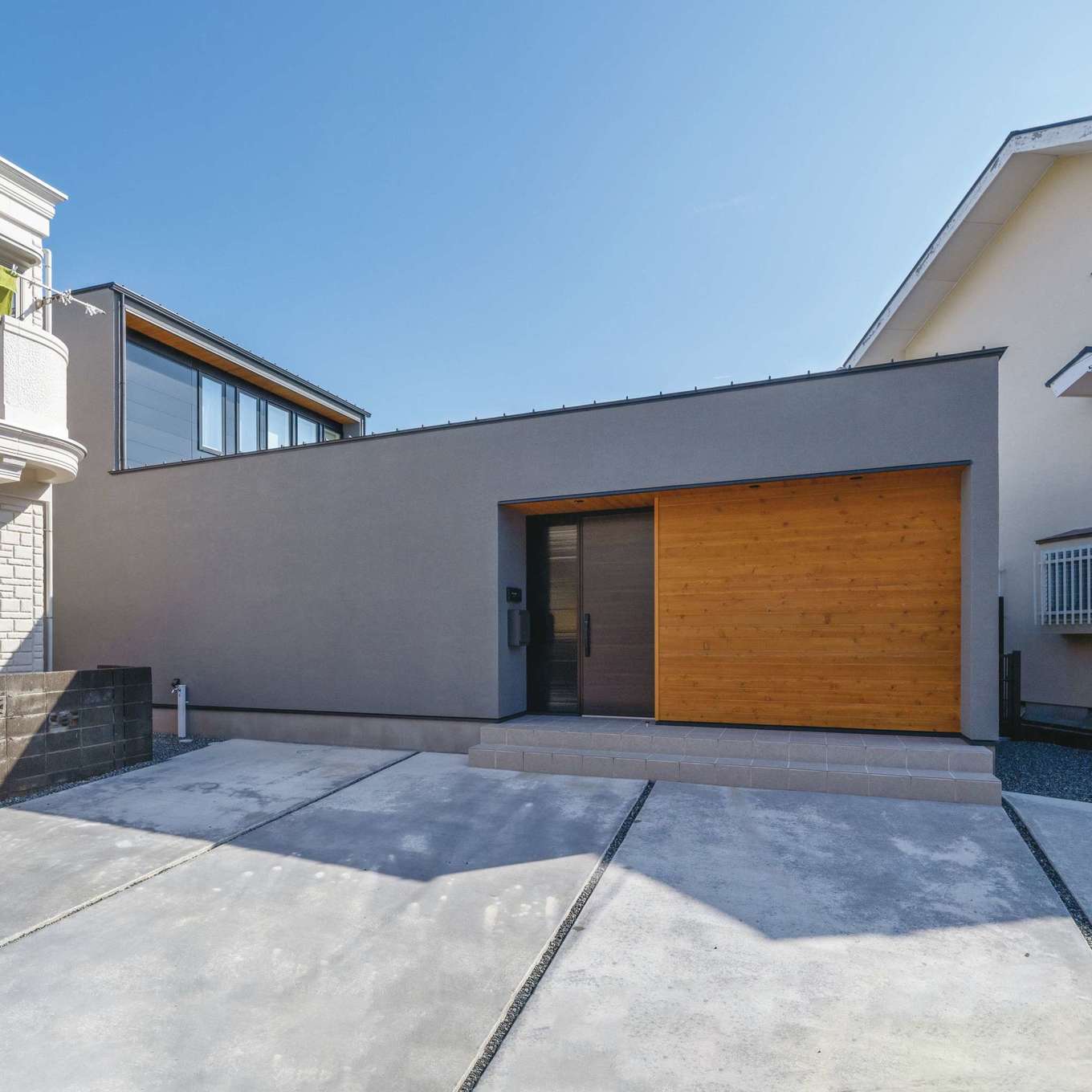 ハウスプラン（R＋house沼津・富士）【デザイン住宅、省エネ、建築家】通りに面した駐車場と玄関。グレーの塗り壁とレッドウッドを組み合わせた、センスを感じるシンプルなデザイン。プライバシーを守りながら、明るさと開放感を確保した室内は快適そのもの。家族だけでのびのび過ごせる庭が、光と風を家の奥へと届けてくれる
