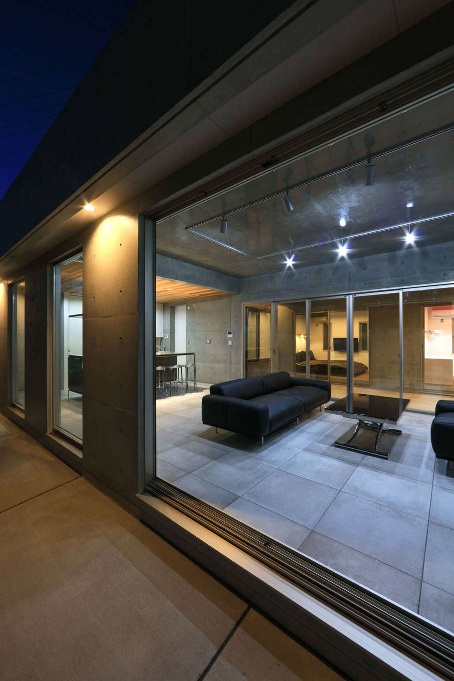 BAUM HOME（岩崎工務店）【デザイン住宅、平屋、鉄骨鉄筋コンクリート構造】ワイドな開⼝が設けられるのもRC造のポイント。ここから⼼地よい⾵と光が室内に取り込める。無機質な空間にモダンな家具を合わせたコーディネートも秀逸