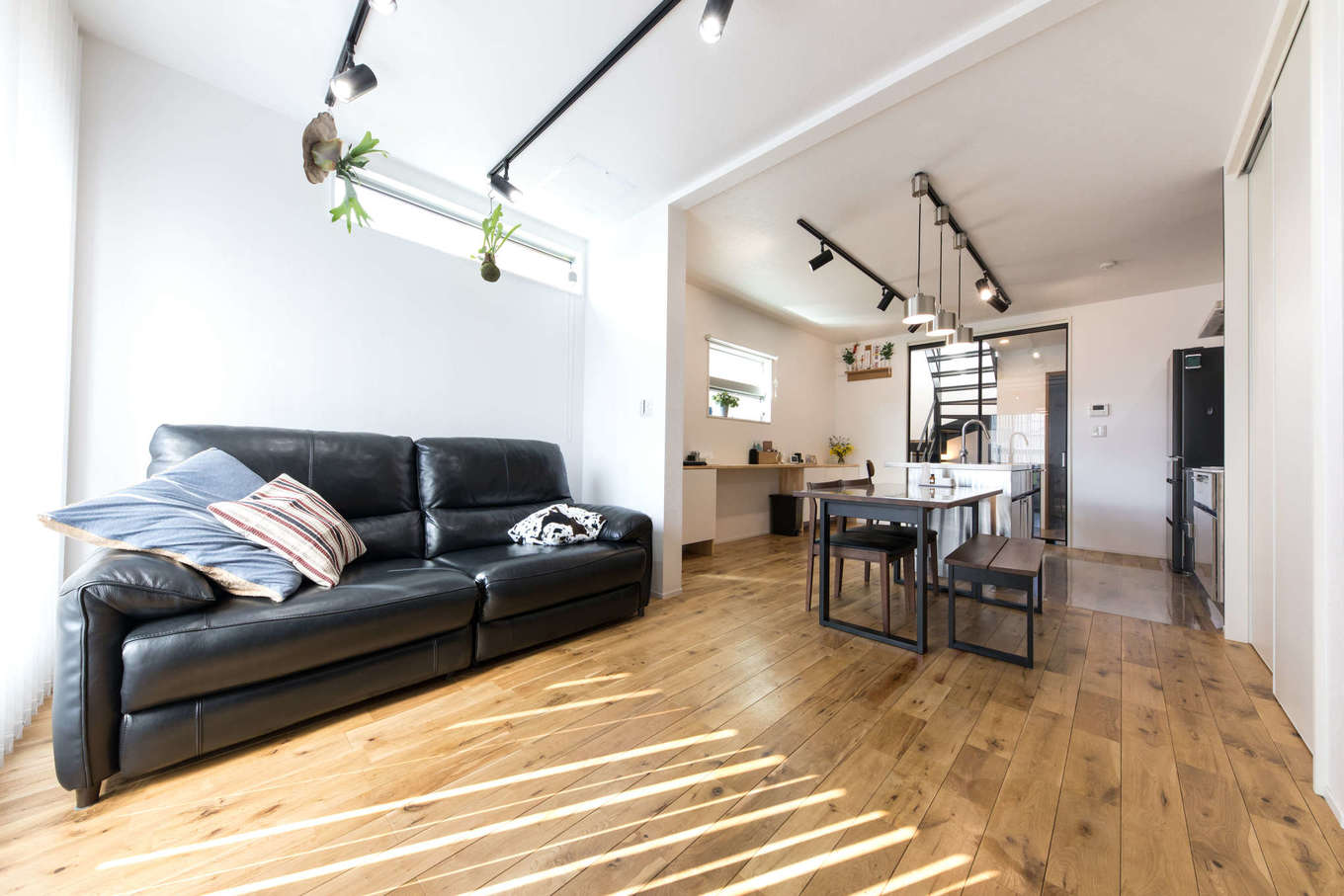 建築システム（狭小住宅専門店）【狭小住宅、間取り、屋上バルコニー】明るい日差しが入る2階リビング。床材にはナラの無垢材を用いて落ち着いた雰囲気に。リビングの照明もスポットライトで個性的に。カフェのようなキッチンは、ステンレスの質感でシャープな印象