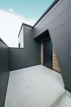 母屋からの視線を遮るために高い塀を設け、なおかつゲストを気持ち良く迎えるために広いアプローチをつくった。ファサードに木目のサイディングを張ってアクセントをつけた