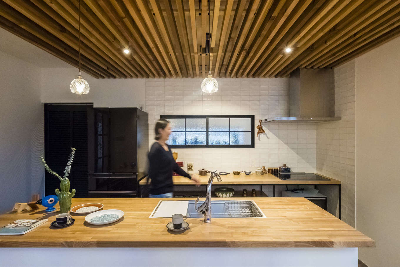 Hands Works（アオイ建築）【デザイン住宅、収納力、自然素材】シンクとコンロを分けたセパレート型のキッチンを造作。ダイニング兼用として使うスタイルで、家族のコミュニケーションもスムーズ。天井の木格子がおしゃれなアクセントに。アイアンの窓枠をつけたバックヤードは広いパントリー