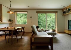 緑の借景を楽しみながら過ごせるLDK。夏の熱気、梅雨の湿気、騒音や匂いなどの問題を外断熱＋換気システムで解消。PM2.5や花粉をシャットアウトしつつ、森のような澄んだ空気が循環する