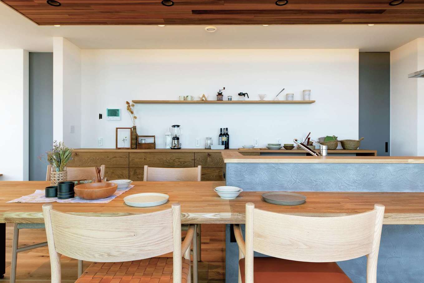 KUREKEN HAUS（榑林建設）【デザイン住宅、自然素材、省エネ】モルタル塗りのキッチンはカフェのよう。横並びのダイニングと正面のカウンターは気分や用途で使い分けられ、利便性も高い。キッチン収納や飾り棚も雰囲気に合わせナラ材を使用した造作
