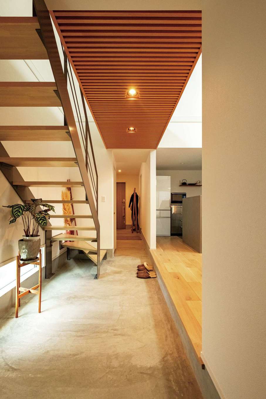 ハートホーム【デザイン住宅、高級住宅、間取り】玄関まで続く一直線の通り土間が室内に開放感をもたらす。渡り廊下の下部分には無垢材の格子をあしらい、木の素材感が無機質な空間にぬくもりを添える