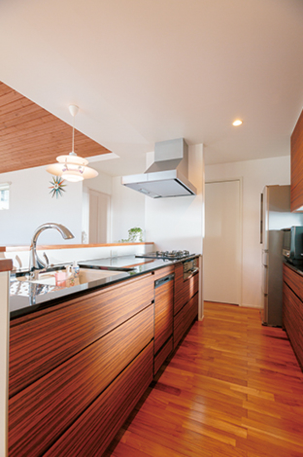 木目のパネルと黒御影石の天板が融合した納得オリジナルキッチン。生活感を出さないために、キレイにたっぷりと収納できるカップボードを設置