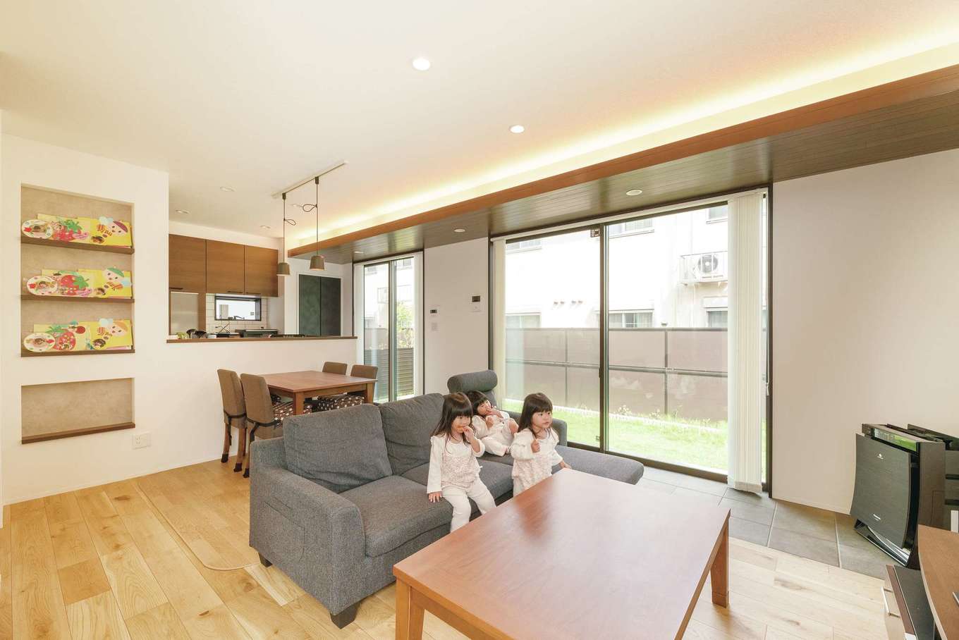 三和建設【子育て、収納力、間取り】キッチンからはリビングや庭が見渡せ、元気に遊ぶ子どもたちに目が届く。キッチンのサブウェイタイルや、間接照明と組み合わせた窓側の木目天井がインテリアのアクセントに