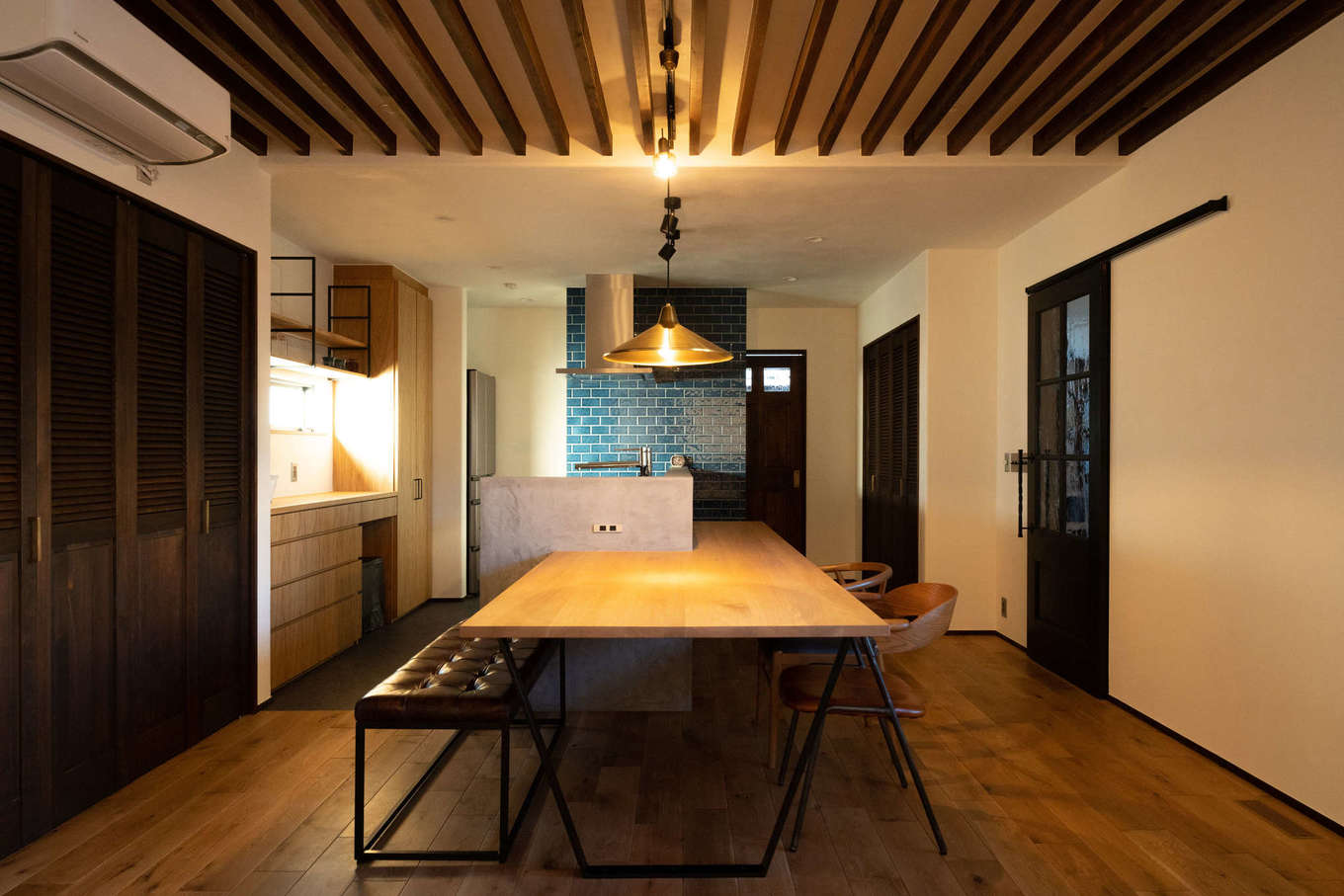 バルハウス【デザイン住宅、自然素材、間取り】ヴィンテージテイストでコーディネートされたLDKは、モールテックスの腰壁で囲んだキッチン一体型のダイニングテーブルがインテリアの主役。ブルーのタイルが空間にポイントを添えている。ルーバー状に仕立てたアクセント天井の陰影が、家族の団らんをやさしく見守る