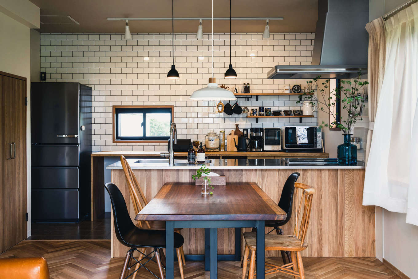 ALAIN（アラン）｜カフェスタイルのオープンキッチン。奥さまのたっての希望で、バックヤードにサブウェイタイルを採用。ペンダントライトはルイス・ポールセン。レンジフードが付いていた垂れ壁を撤去したことで開放感が生まれた。ワークトップ、冷蔵庫、ダッシュBOXをステンレス製にして統一感を出した