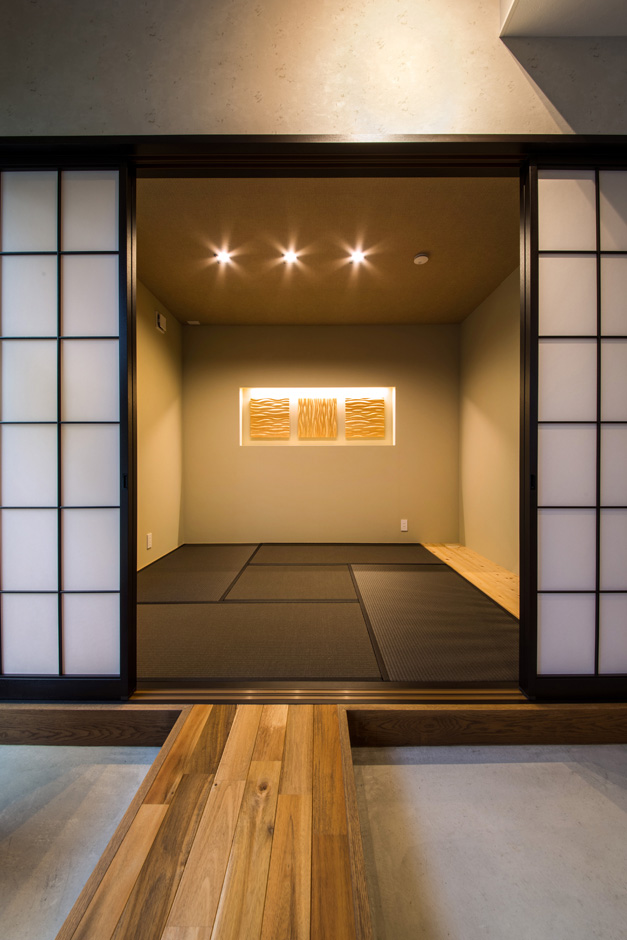 SEIEN ARCHITECT【デザイン住宅、建築家、インテリア】壁に木のパネルのオブジェを飾り、旅館の一室のように洗練された和室。ダイニングとの間に廊下を渡してある。障子を黒枠にしたことで、閉めたときの印象がインダストリアルなダイニングと違和感なく調和する