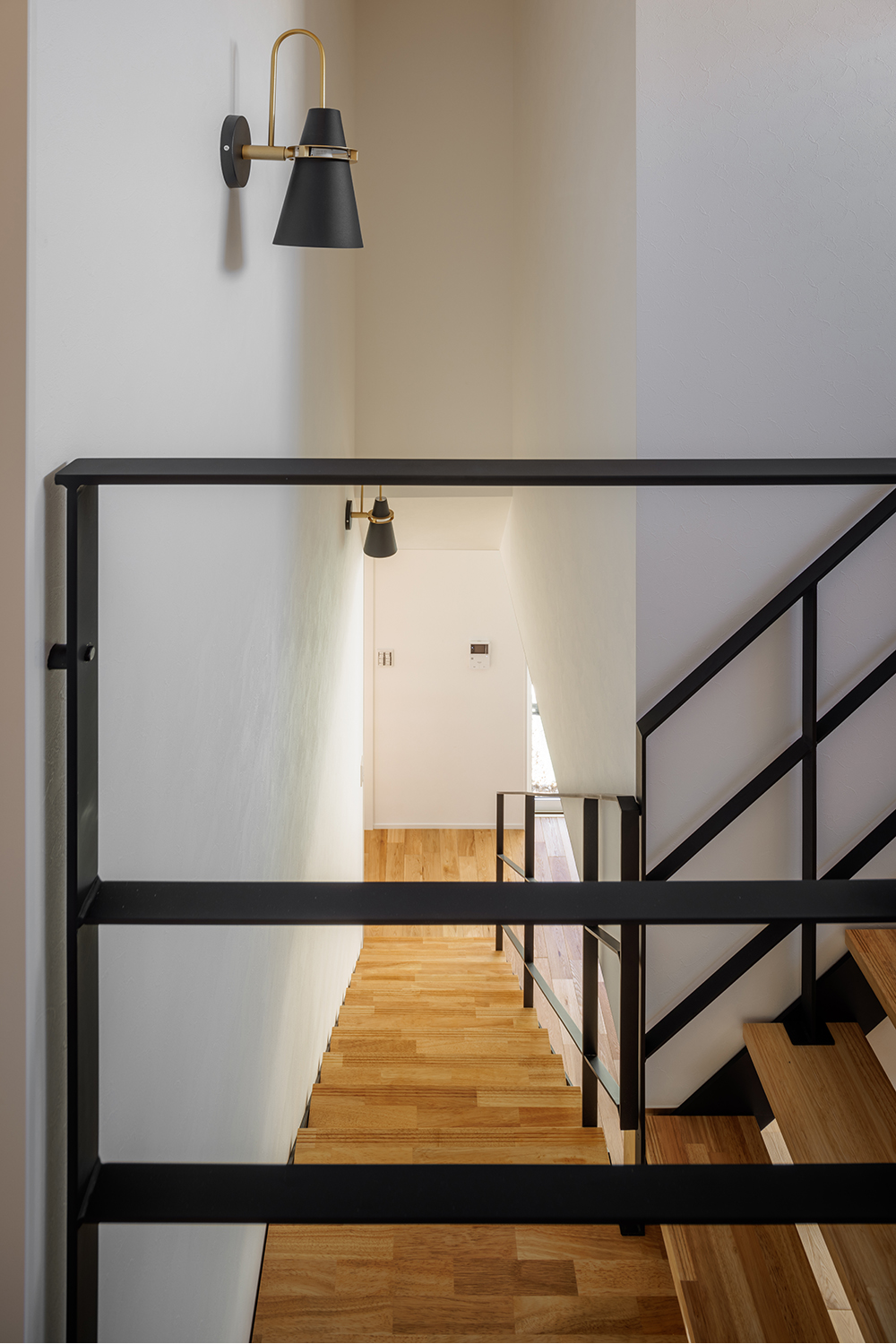 tact design firm【デザイン住宅、子育て、間取り】黒い手すりが印象的なシンプルかつモダンな階段。壁にはおしゃれな照明が設置されており、温かみのある空間に