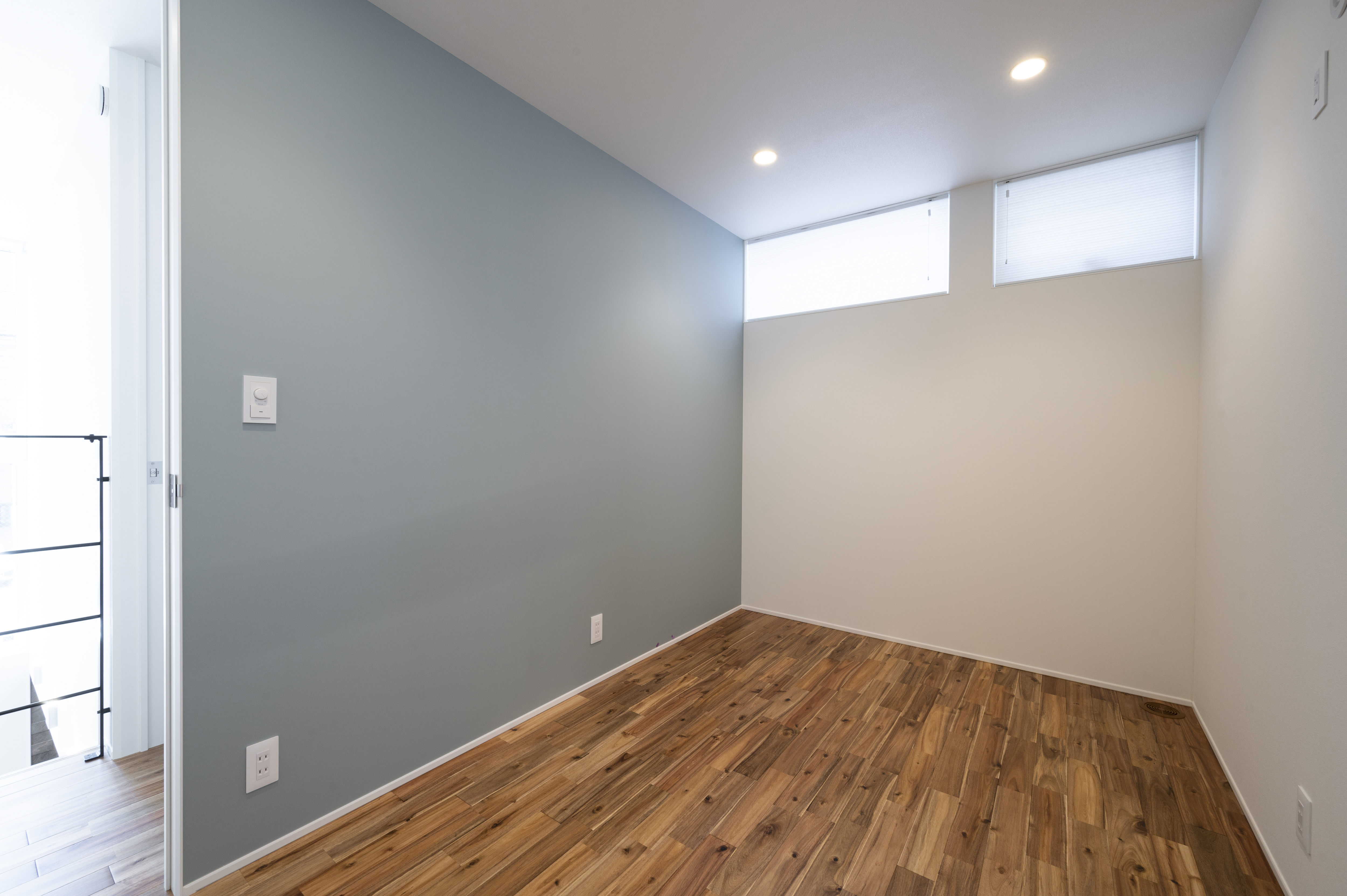 オネストアーク｜シンプルで落ち着いた雰囲気の居室。木目調のフローリングとグレーのアクセントウォールが調和している。