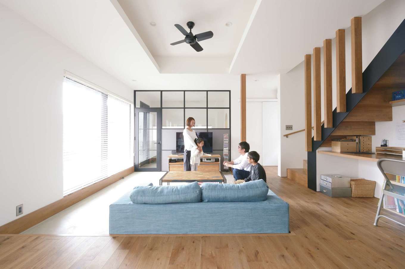 MABUCHI【デザイン住宅、狭小住宅、建築家】モルタル仕上げの土間玄関からそのままフラットにつながるピットリビング。“おこもり”感があるので、家族みんなが自然に集まってくる。ダイニングキッチンからフロアダウンさせたことで、空間に変化が生まれた。吹抜けの代わりに折り上げ天井を採用し、その上が小上がりの畳コーナー。アイアンに見える黒いフレームの間仕切りがシンプルな空間を引き締めると同時に、ギャラリーのような佇まいを見せている