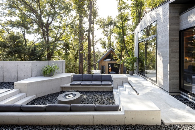 自然に囲まれたモダンなテラス。コンクリート製のベンチとファイヤーピットがあり、くつろぎの空間を提供する。