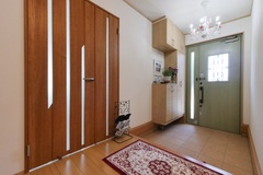 木目調のドアとタイルの組み合わせが美しい玄関。大きなシャンデリアが高級感を演出し、招かれる印象を与える。