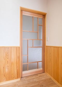 繊細なデザインのガラス入り引き戸が通路に上品さを加えている。自然素材を活かした壁とのコントラストが美しい