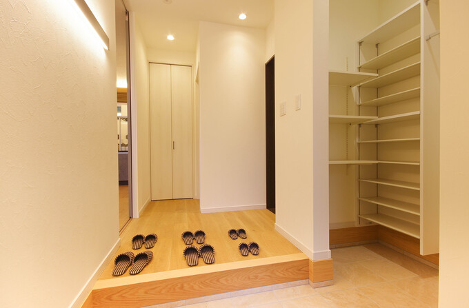 清潔感のある玄関ホール。スリッパが整然と並び、右側には十分な収納スペースを備えたシューズラックが配置されている。