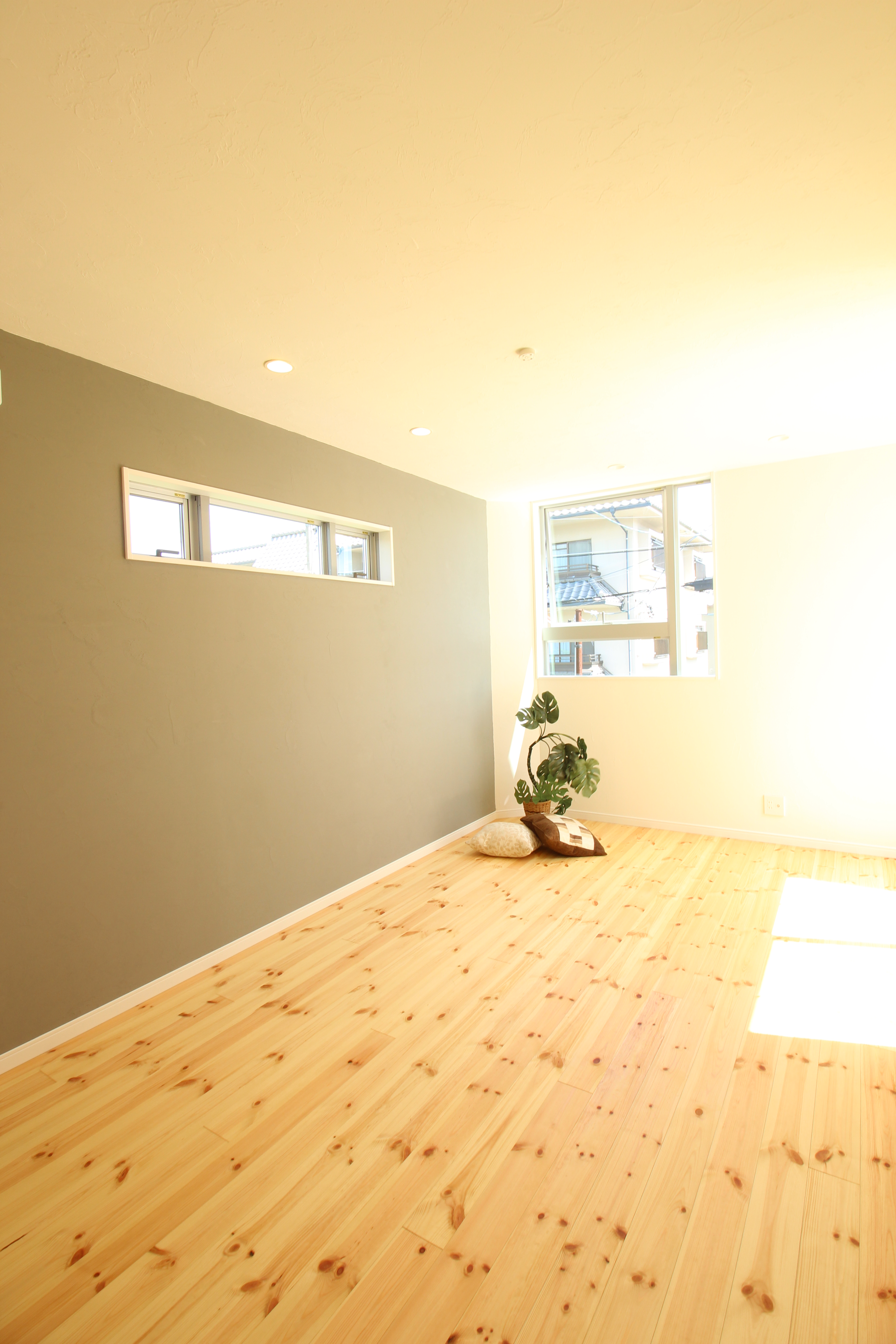 小野田産業～designers house project～｜窓から差し込む自然光が心地良い居室。シンプルなデザインが部屋の広さを感じさせ、壁際の観葉植物がアクセントになっている。